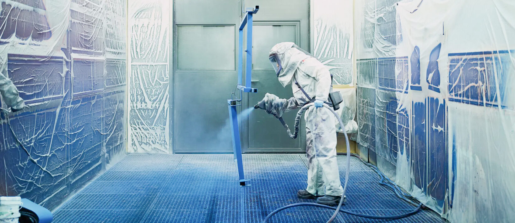 Dieses Bild zeigt einen Mann in einem Schutzanzug, der Metallteile Blau an sprayt.